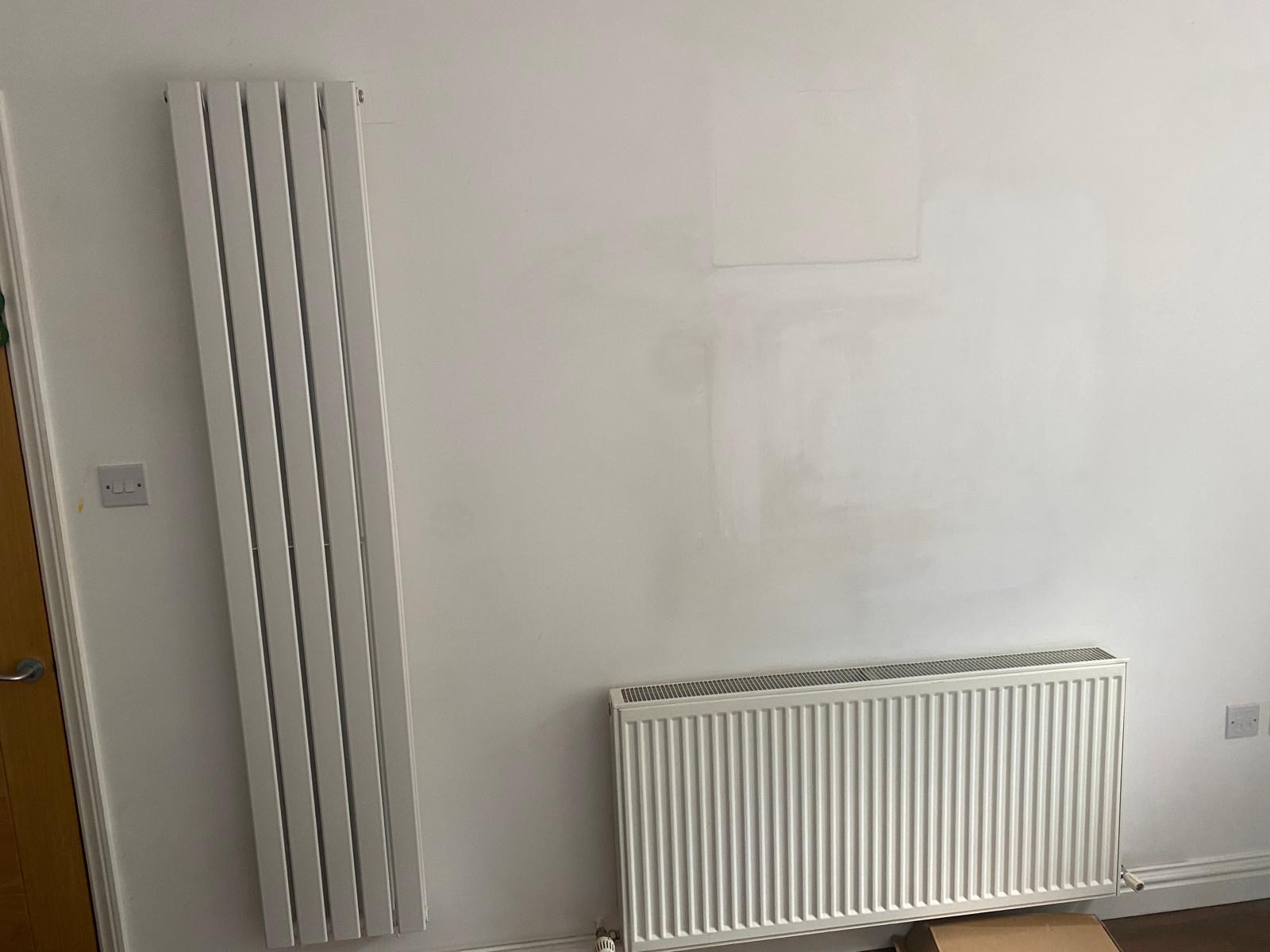 New radiators fitted — a vertical designer panel and a horizontal convector, walls made good around them.
